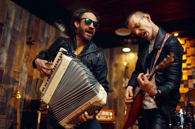 Dos artistas brutales con acordeón y balalaika, tocando música en el escenario. Rendimiento de la banda de rock o repetición en el garaje, hombre con instrumento musical, sonido en vivo