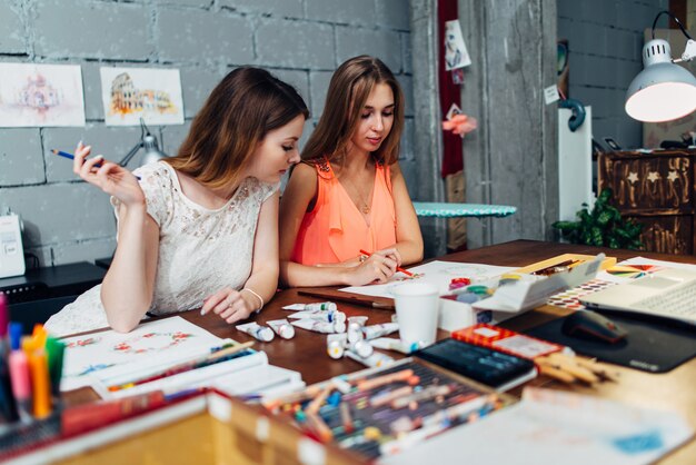 Dos artistas femeninas dibujando elementos decorativos sentado en el escritorio en estudio creativo