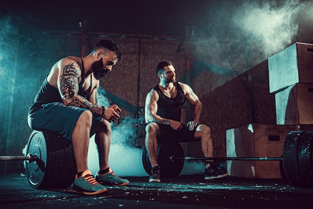 Dos atletas tatuados con barba muscular que entrenan en el gimnasio
