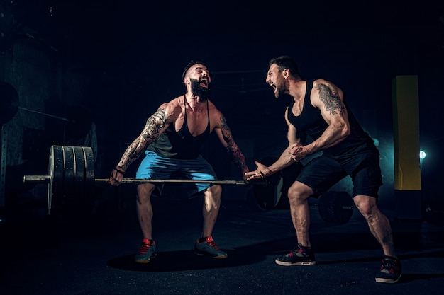 Dos atletas tatuados con barba muscular que entrenan en el gimnasio