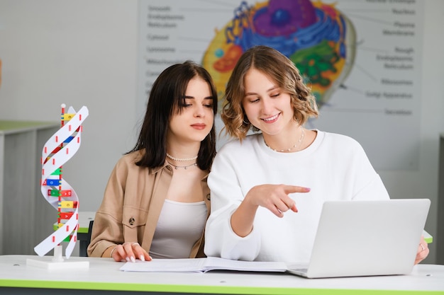 Dos atractivas estudiantes de secundaria se sientan en el escritorio con una computadora portátil y un cuaderno