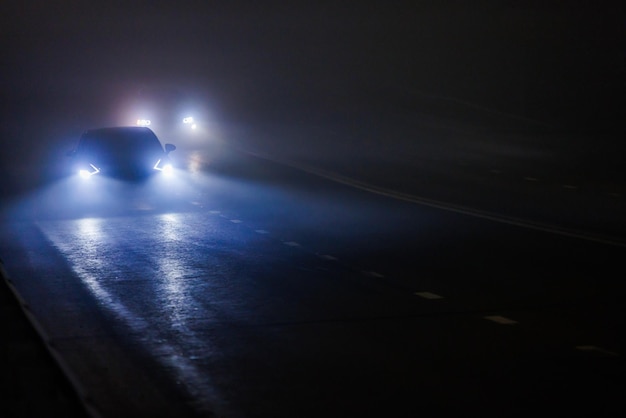 Dos autos borrosos moviéndose en un camino nublado de noche vacía