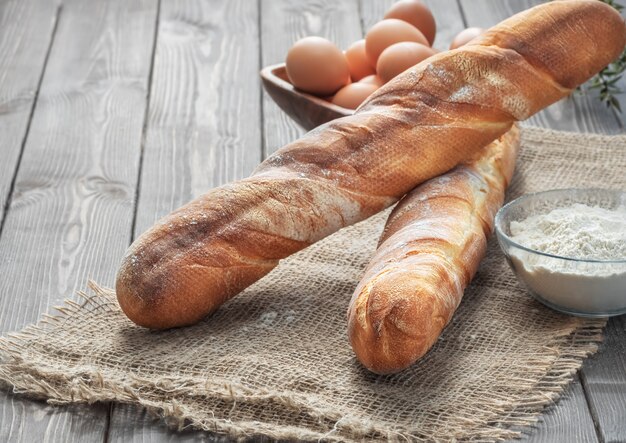 Dos baguettes francesas frescas hechas de harina blanca junto a huevos de gallina y harina