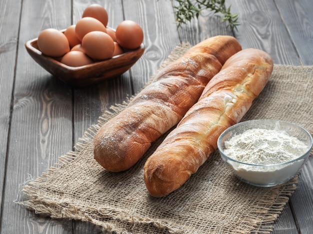 Dos baguettes francesas frescas hechas de harina blanca junto a huevos de gallina y harina