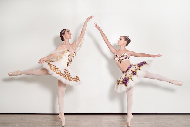 Dos bailarinas practicando poses de ballet sobre un fondo blanco.