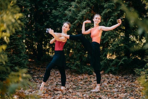 Dos bailarinas sonrientes posando divertidas y tomando selfie con caras emocionales en el parque.