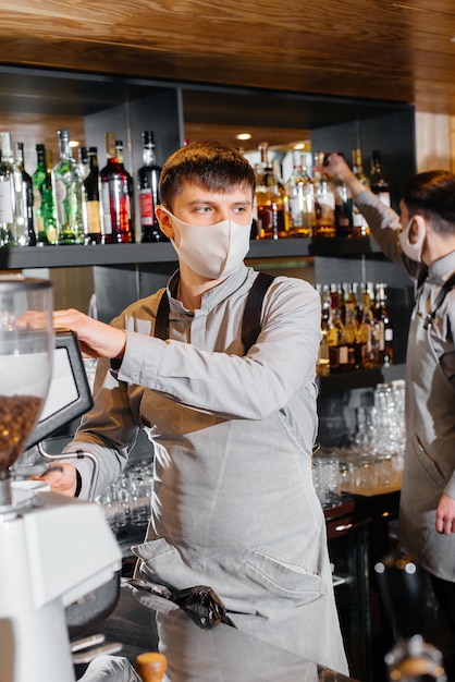 Dos baristas enmascarados preparan un delicioso café en el bar cafetería. El trabajo de los restaurantes y cafés durante la pandemia.