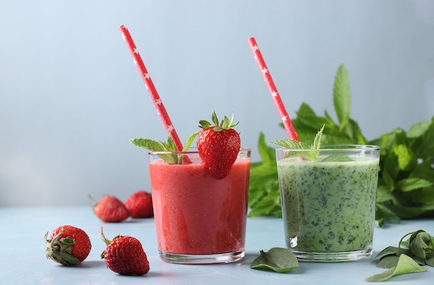 Dos batidos de desintoxicación saludable con fresas frescas, espinacas, menta y yogur en vasos sobre fondo azul claro