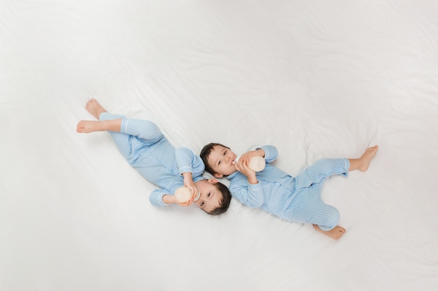 Dos bebés gemelos en pijama yacen en la cama bebiendo leche de biberones. Vista desde arriba. concepto de matrimonio y amistad. concepto de comida para bebés espacio para texto