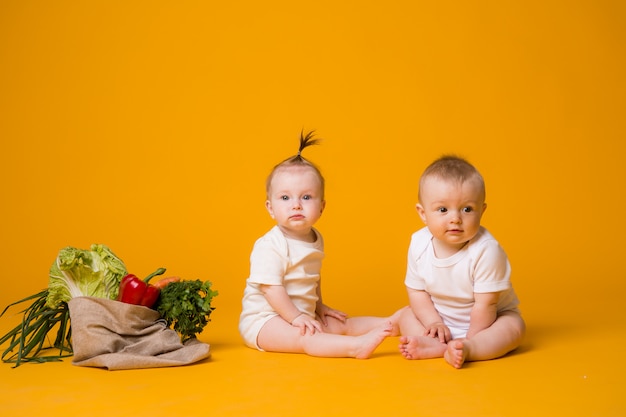 Dos bebés y una niña rodeados de verduras frescas en una bolsa ecológica en naranja