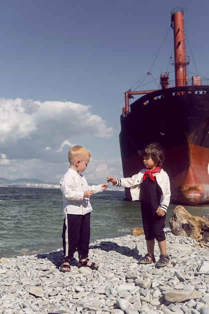 Foto dos bebés varones de moda junto a un gran barco de río que encalló frente a novorossiysk