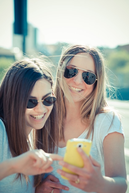 dos bellas mujeres jóvenes que usan teléfonos inteligentes