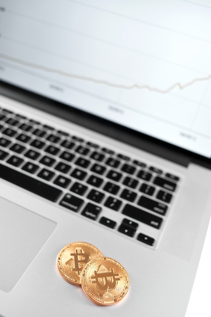 Dos bitcoins dorados colocados en una computadora portátil plateada con un cuadro financiero en su pantalla