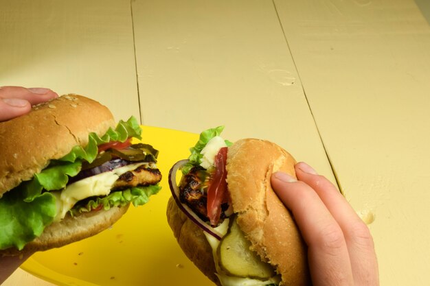 Dos bocadillos con diferentes rellenos en las manos sobre un fondo claro de madera.