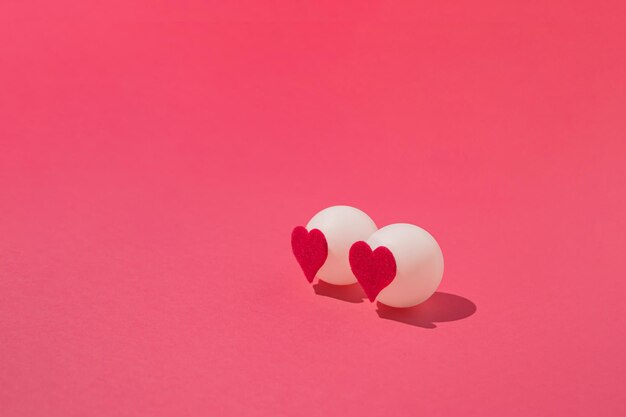 Foto dos bolas blancas de ping ping con corazones de fieltro sobre fondo rosa concepto mínimo de amor o san valentín
