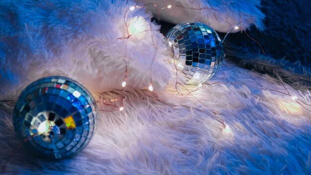 Dos bolas de discoteca acostadas sobre una acogedora manta con guirnalda de luces navideñas. Interior de una casa acogedora. Hogar dulce hogar. Después de la fiesta. Decoración de año nuevo.