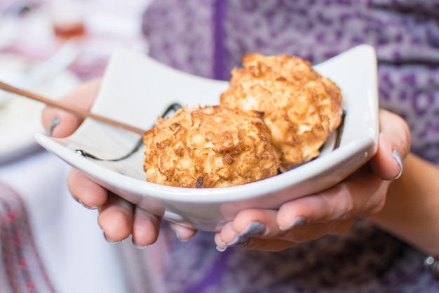 Dos bolas de helado frito vertidas con jarabe de chocolate en un plato blanco en manos femeninas