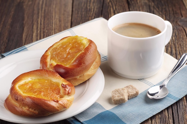 Dos bollos dulces con mermelada y taza de café en la mesa de madera antigua