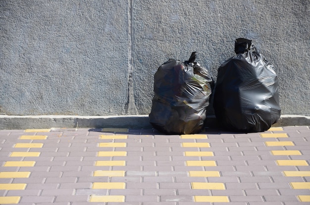 Dos bolsas de basura negras en el piso de la calle de azulejos en la cerca de concreto en la ciudad