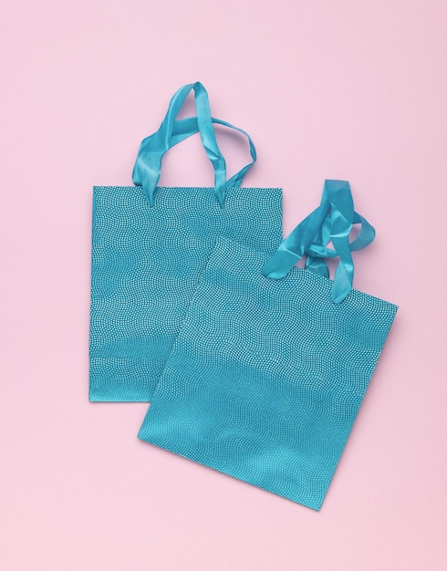 Dos bolsas de regalo azules brillantes en un fondo rosado
