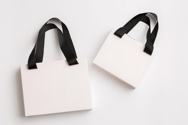 Dos bolsas de regalo de papel blanco con asas negras sobre fondo blanco
