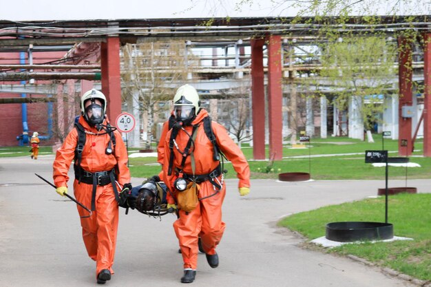 Dos bomberos profesionales con trajes ignífugos de protección naranja, cascos blancos y gas
