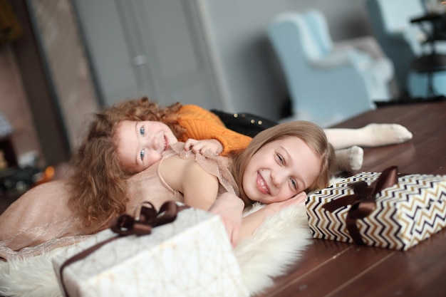 Dos bonitas hermanas tendidas en el suelo en una acogedora sala de estar.