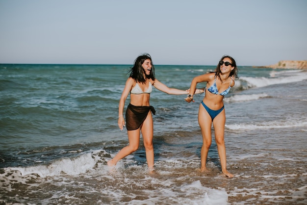 Foto dos bonitas mujeres jóvenes divirtiéndose en la orilla del mar en un caluroso día de verano.