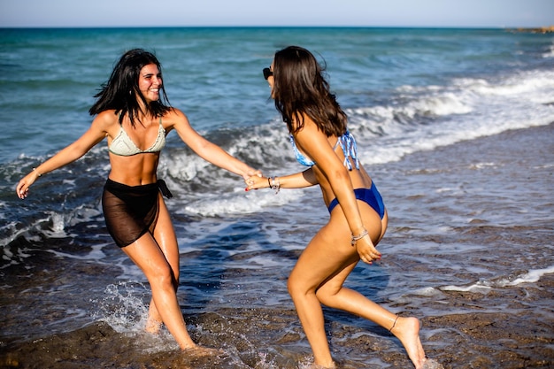 Dos bonitas mujeres jóvenes divirtiéndose en la orilla del mar en un caluroso día de verano.