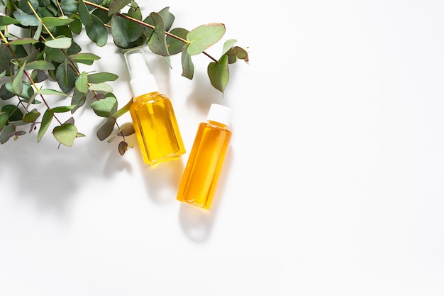 Dos botellas de aceites esenciales orgánicos y ramitas de eucalipto fresco sobre fondo blanco.