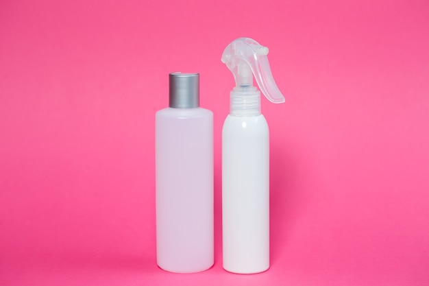 Dos botellas blancas con champú para el cabello, gel corporal, spray para la piel sobre un fondo rosa