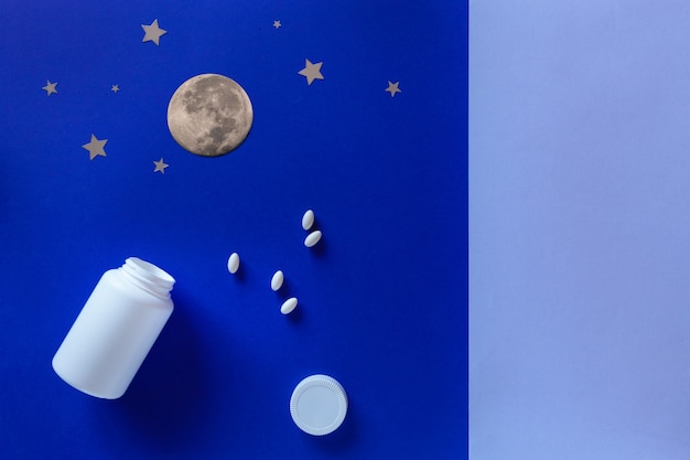 Dos botellas blancas, pastillas, luna sobre fondo azul. Concepto Insomnio, luna llena, problemas de sueño, somnolencia. Maqueta, vista superior, endecha plana, espacio de copia.