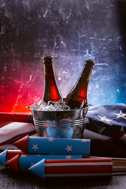 Dos botellas de cerveza en un cubo de hielo con la bandera estadounidense cerca y cohetes para fuegos artificiales. Concepto de celebración del día de la independencia