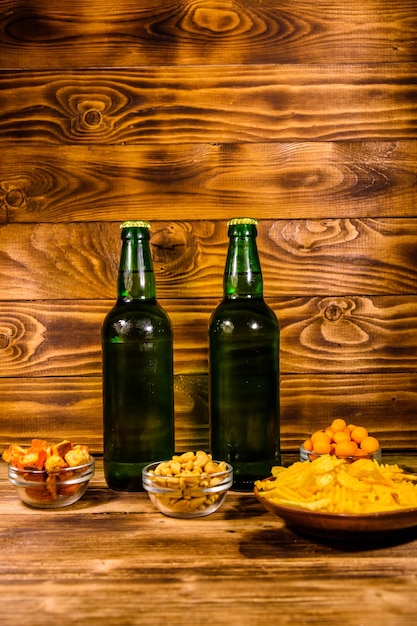 Dos botellas de cerveza y diferentes bocadillos en mesa de madera.