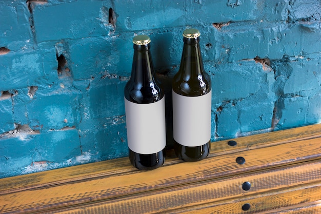 Dos botellas de cerveza con etiquetas en blanco se colocan en un soporte de madera en el fondo de una pared de ladrillo