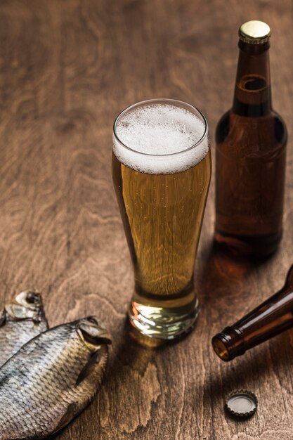 Dos botellas de cerveza oscura, un vaso de cerveza y espuma, pescado seco sobre un fondo de madera.