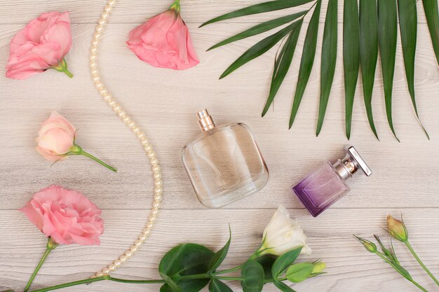 Dos botellas de perfume, perlas en una cuerda, flores blancas y rosadas, hojas verdes sobre fondo de madera. Cosméticos para mujeres. Vista superior.