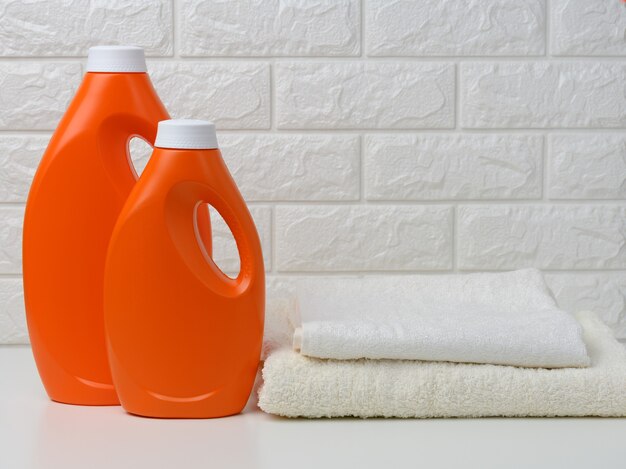 Dos botellas de plástico naranja de detergente líquido y una pila de toallas en un estante blanco, lavado en casa