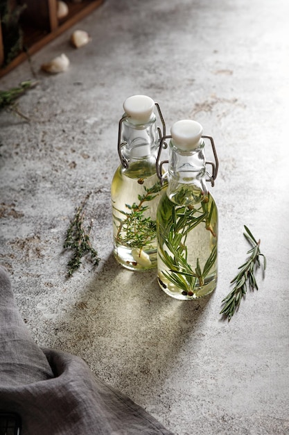 Dos botellas de vidrio de aceite con romero, tomillo y ajo y ramitas de hierbas sobre un fondo gris con una servilleta