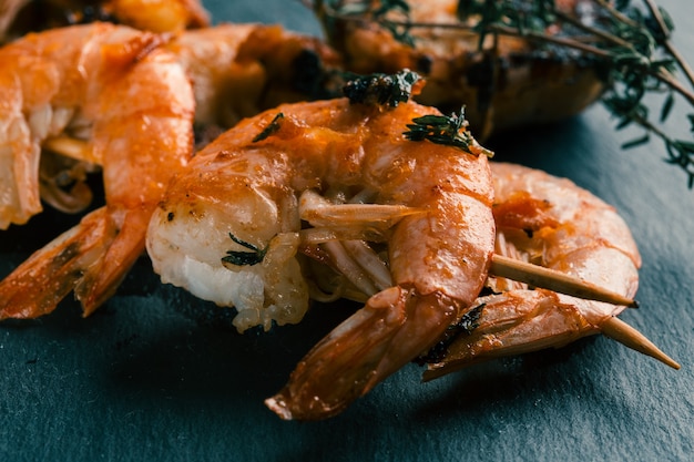 Dos brochetas de camarones fritos con ramitas de tomillo sobre la pizarra negra