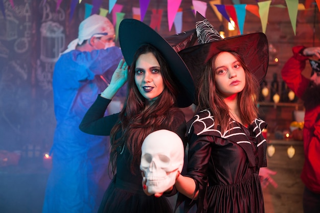 Foto dos brujas en un halloween celebrando sosteniendo un cráneo humano. brujas alegres. mirando a la cámara.