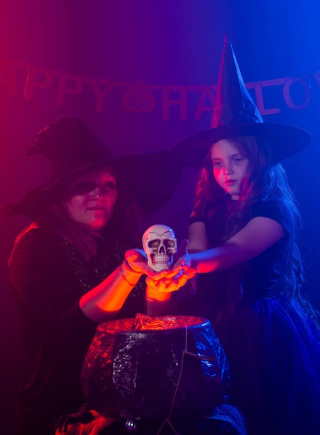 Foto dos brujas de halloween haciendo una poción y conjurar con el cráneo en la noche de halloween vacaciones mágicas y concepto místico