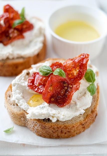 Dos bruschettas con aceitunas de queso ricotta y tomates secos en pan ciabatta sobre fondo blanco.