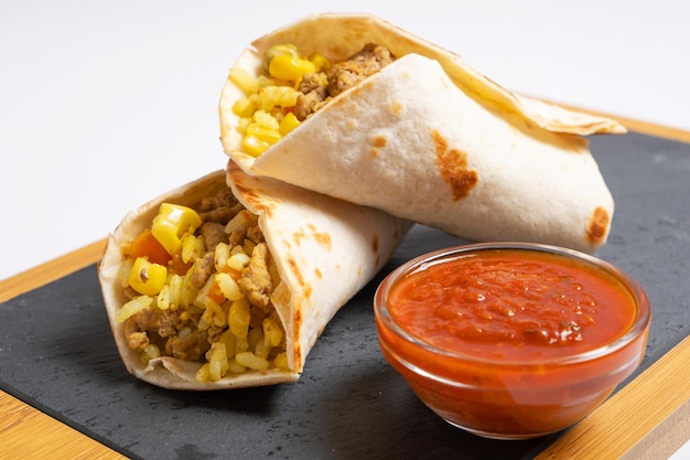 Dos burritos yacen en una tabla para servir junto a una salsa de tomate picante cocina mexicana