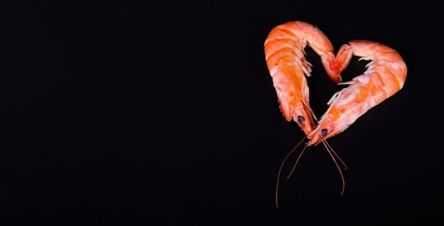 Dos camarones que forman un corazón en un fondo negro.