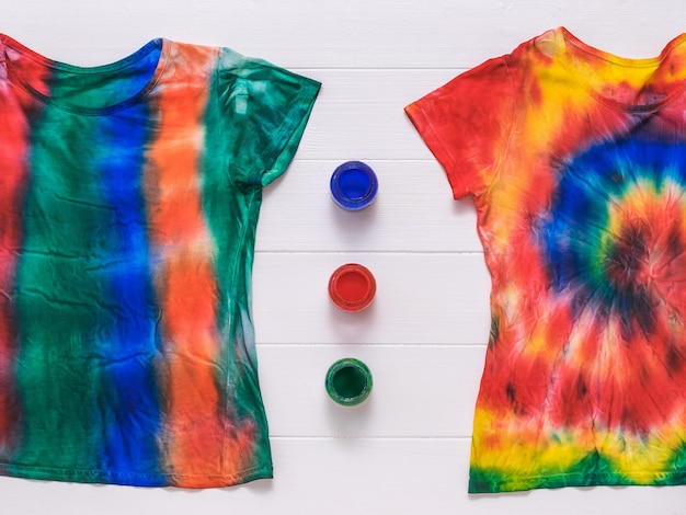 Foto dos camisetas tie dye y pintura sobre una mesa blanca lay flat