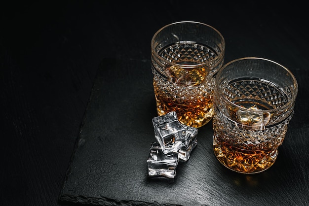 Dos caros vasos de whisky con hielo en una bandeja de piedra negra