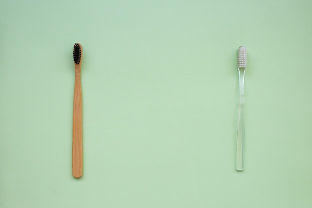 Dos cepillos de dientes: bambú natural y plástico sobre un fondo de papel verde.