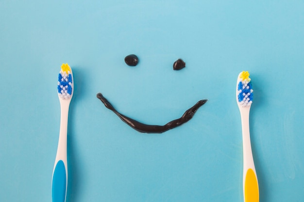 Dos cepillos de dientes de color plástico y un tubo de sonrisa divertida de una pasta de dientes negra