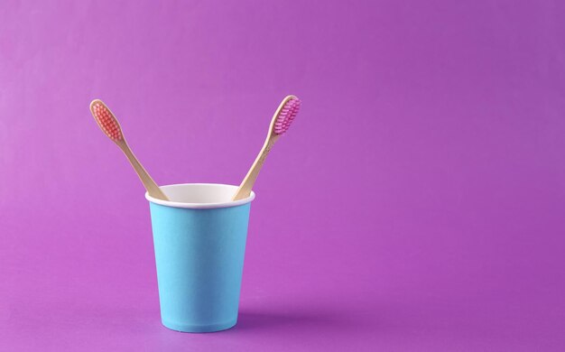 Dos cepillos de dientes ecológicos en taza sobre fondo morado Cuidado dental